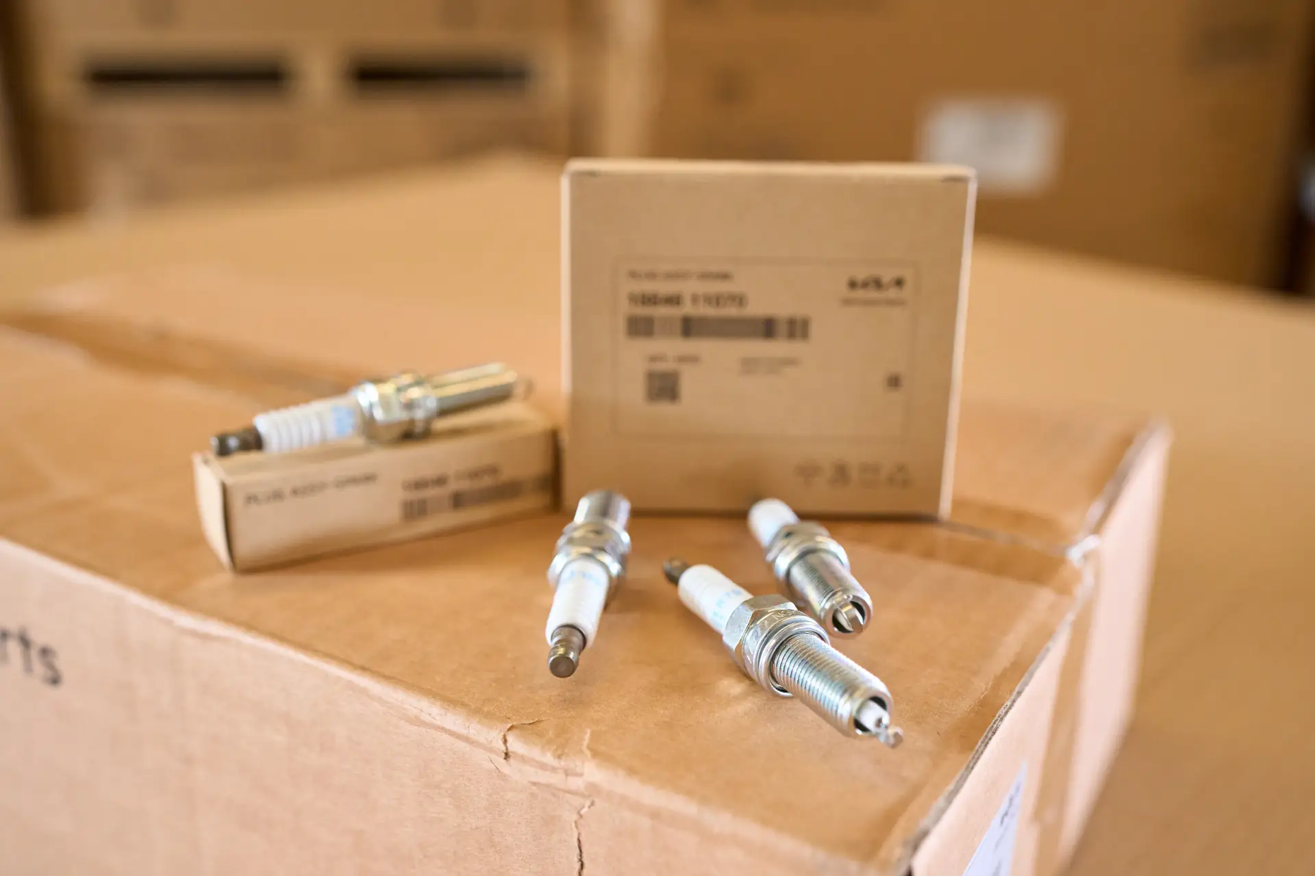 Close-up of genuine spark plugs and their boxes resting on a parts carton